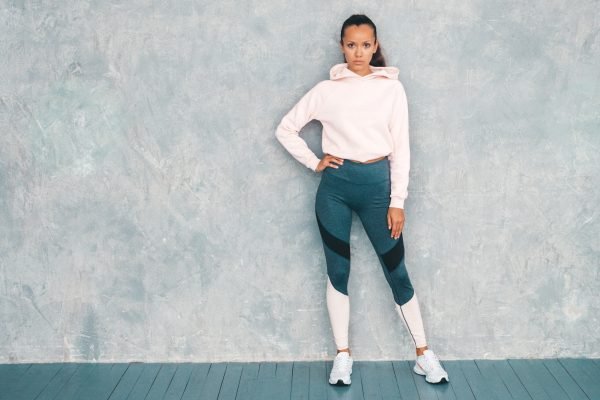 Portrait of fitness woman in sports clothing looking confident.Young female wearing sportswear. Beautiful model with perfect tanned body.Female posing in studio near gray wall